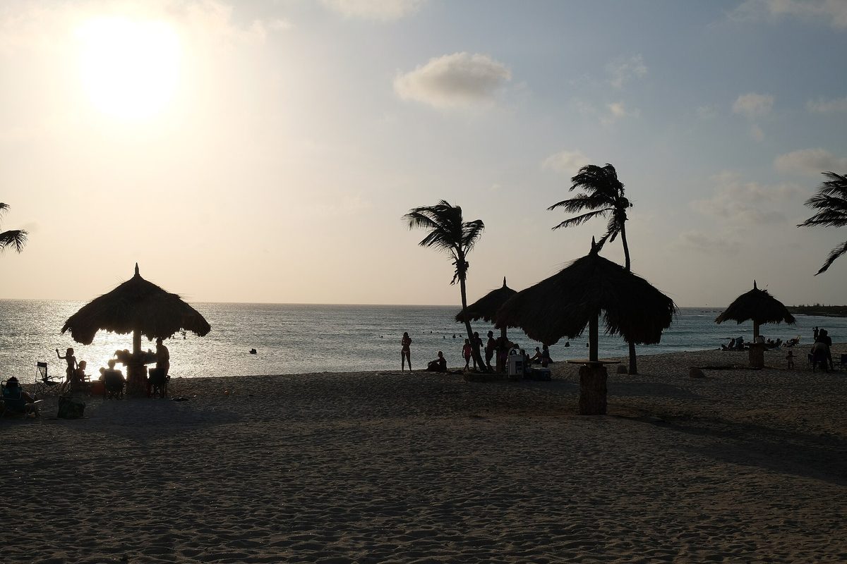 Aruba beach with palapas at sunset where happy-hour drink prices drive the all-inclusive math