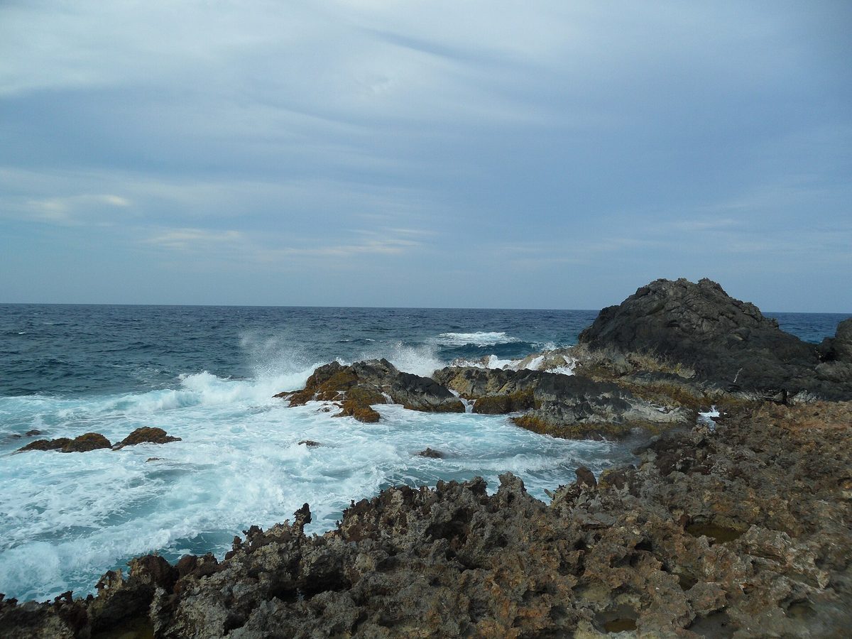 Waves crashing over jagged volcanic rocks along Aruba's rough northeastern coast near the Natural Pool, where swimming outside the sheltered basin is dangerous