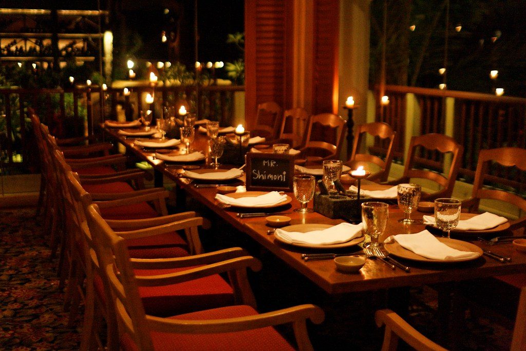 A candlelit dinner on the beach Aruba couples love, a long table set in the sand glowing under string lights at dusk