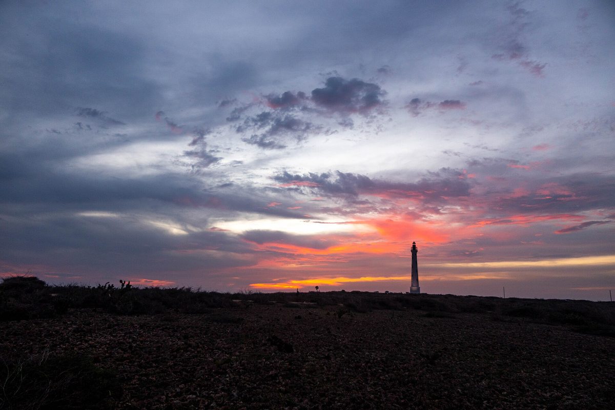 Sunset view of the California Lighthouse silhouetted against a pink and orange sky on Aruba's northwest coast