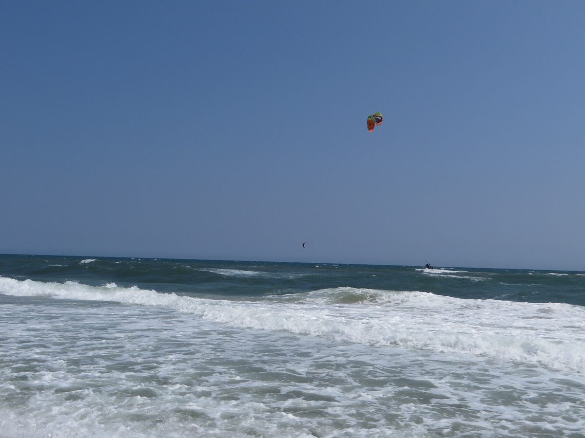 Kiteboarder riding open ocean swell beneath a bright blue sky