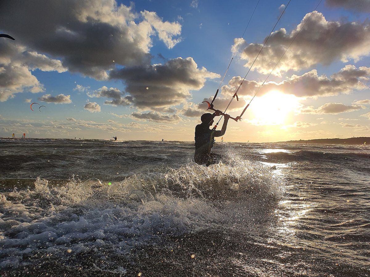 Kitesurfer carving through spray with a power kite overhead at sunset