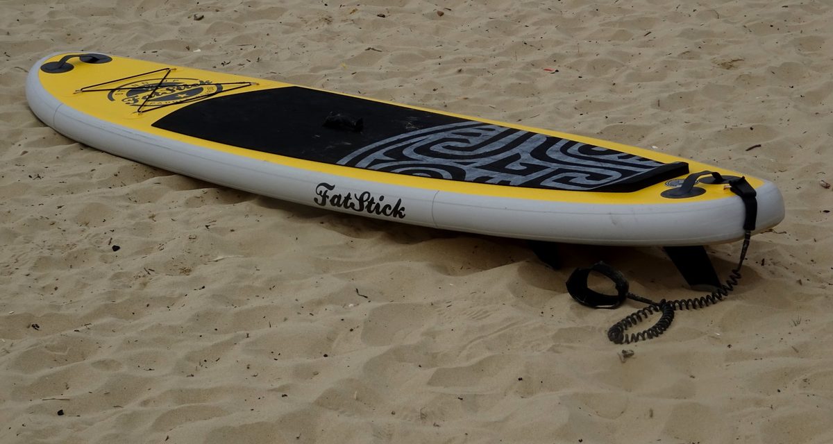 A stand-up paddleboard with its leash on the sand, ready for a calm morning SUP session
