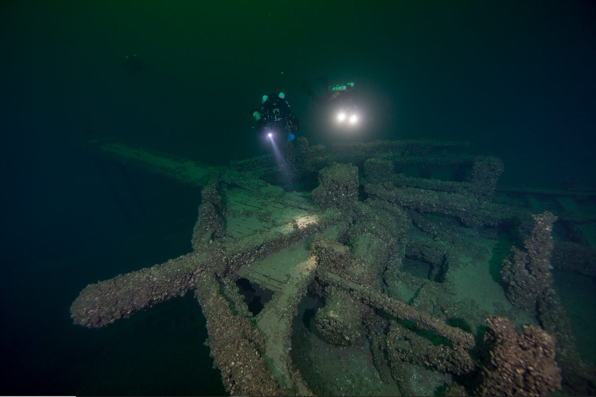An underwater shipwreck encrusted with growth and explored by divers