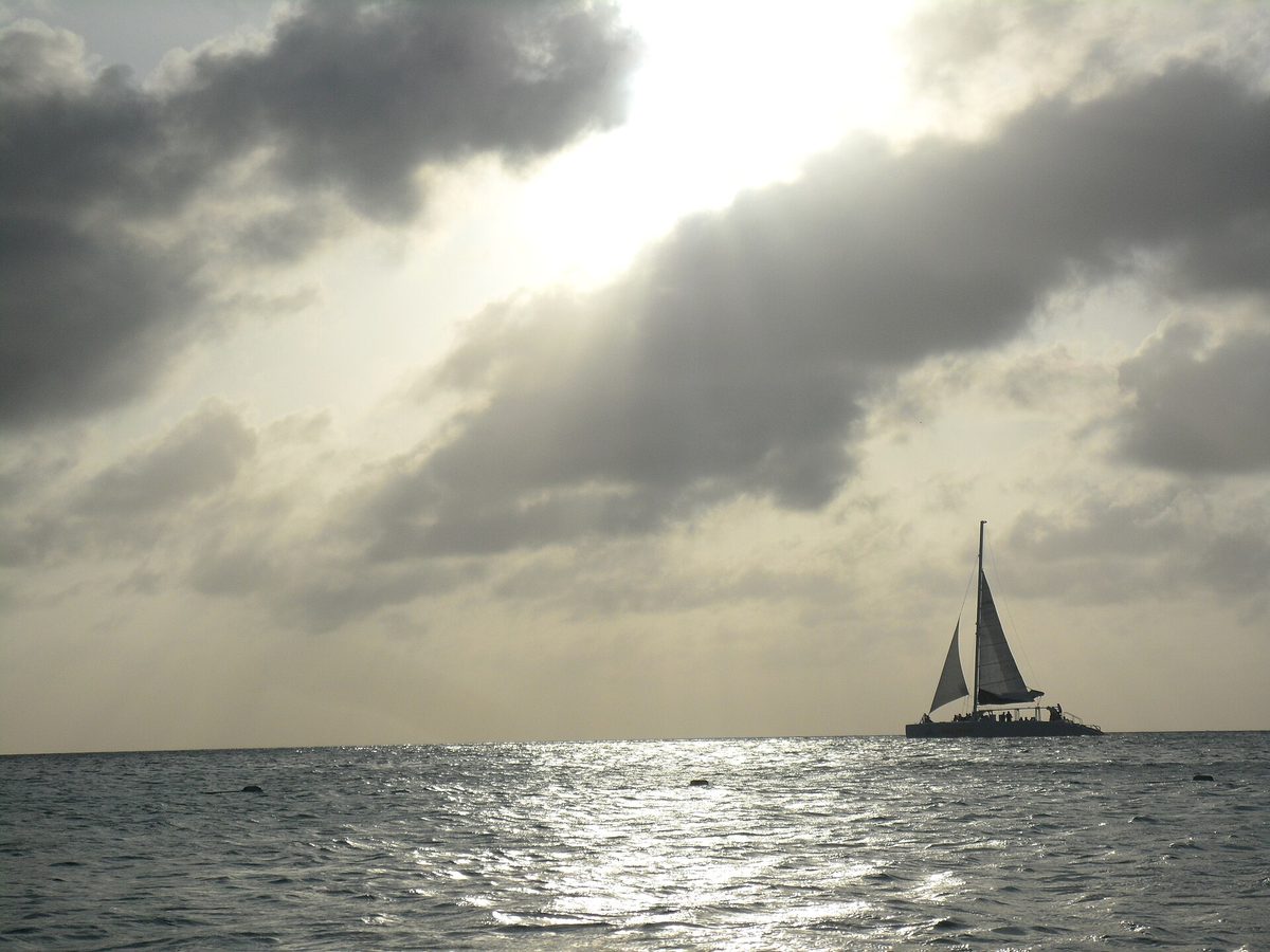 A catamaran sailing on turquoise water off Aruba at golden hour, a typical mid-week excursion expense