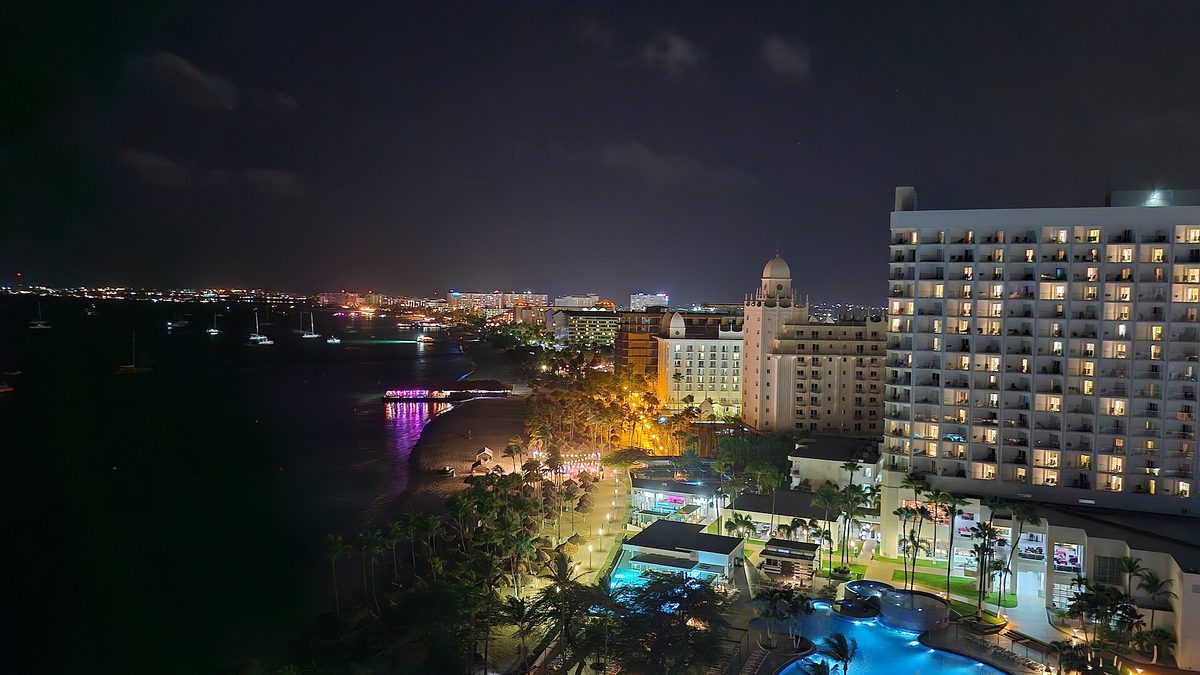 High-rise resorts lit up along Palm Beach in Aruba at night, the priciest lodging tier and the biggest driver of the cost of 7 day trip to aruba