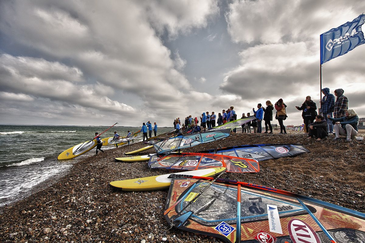 Windsurf boards and rigged sails lined up on the beach with riders gathered